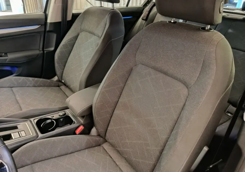 Gros plan sur les sièges avant gris tissu de la Volkswagen Golf 2022, avec accoudoir central et console moderne.