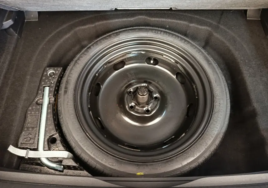 Roue de secours noire et outil de levage visibles dans le coffre d'une Volkswagen Golf gris foncé 2022.