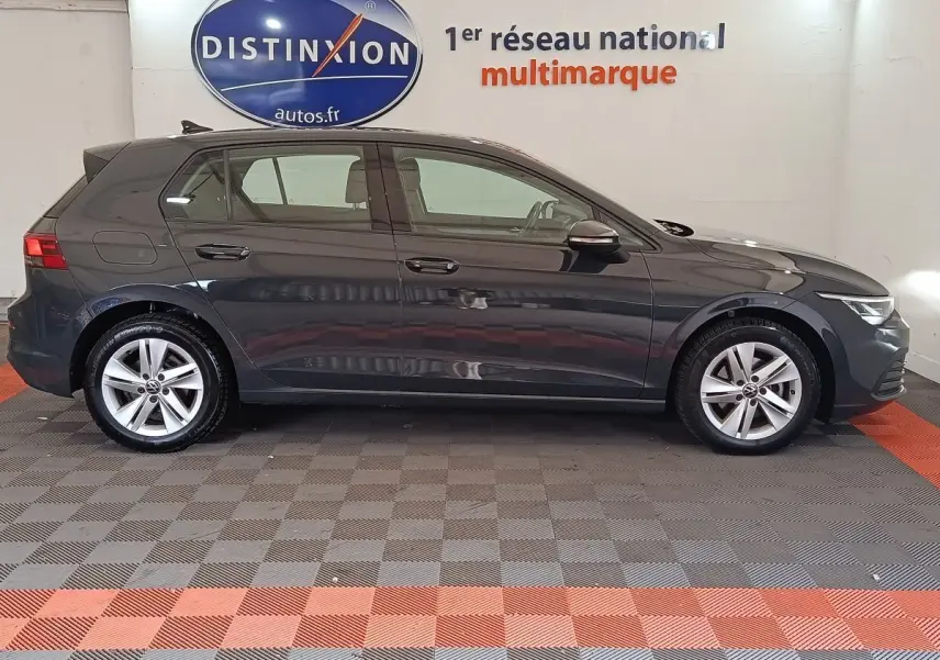 Profil côté gauche d'une Volkswagen Golf gris foncé 2022 en hybride essence, sur sol damier intérieur showroom.