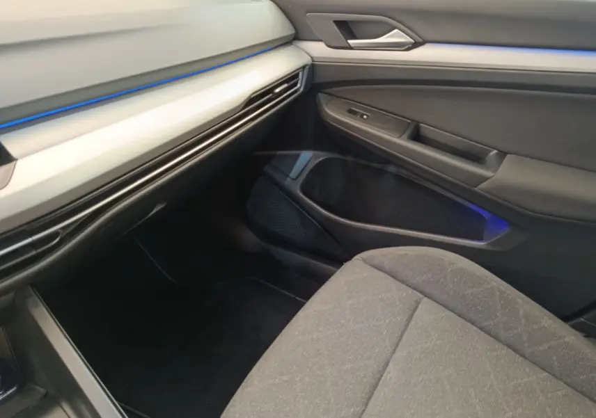 Intérieur côté passager de la Volkswagen Golf gris foncé 2022, avec éclairage d'ambiance bleu et sièges tissu.