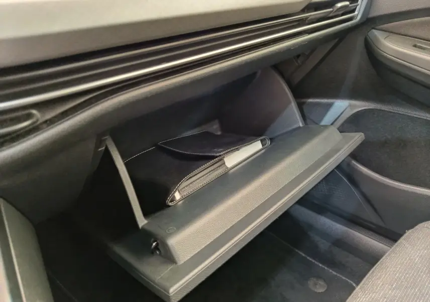 Gant de boîte à gants ouvert côté passager dans une Volkswagen Golf gris foncé, avec pochette noire visible.