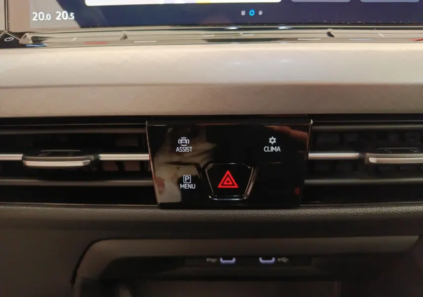 Gros plan sur la console centrale noire de la Volkswagen Golf gris foncé 2022, avec boutons d'assistance, climatisation et alerte.