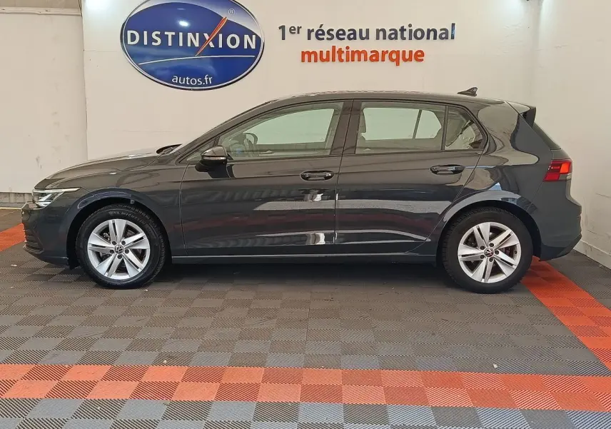 Profil droit d'une Volkswagen Golf gris foncé 2022 exposée en intérieur sur sol damier gris et rouge.