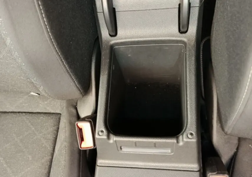 Vue plongeante sur la console centrale noire avec rangement ouvert et prises 12V entre les sièges avant gris foncé d'une Volkswagen Golf 2022.