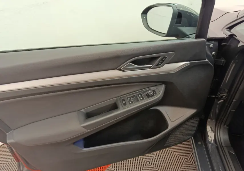 Porte côté conducteur ouverte d'une Volkswagen Golf gris foncé, montrant les commandes électriques et la poignée intérieure.