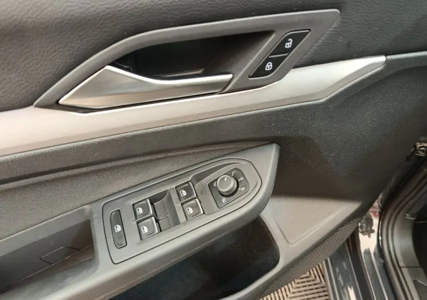 Vue rapprochée de la porte avant gauche grise d'une Volkswagen Golf 2022, avec commandes électriques et poignée argentée.