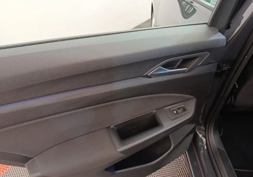 Gros plan sur la porte intérieure côté gauche de la Volkswagen Golf gris foncé, avec poignée et commande de vitre électrique.