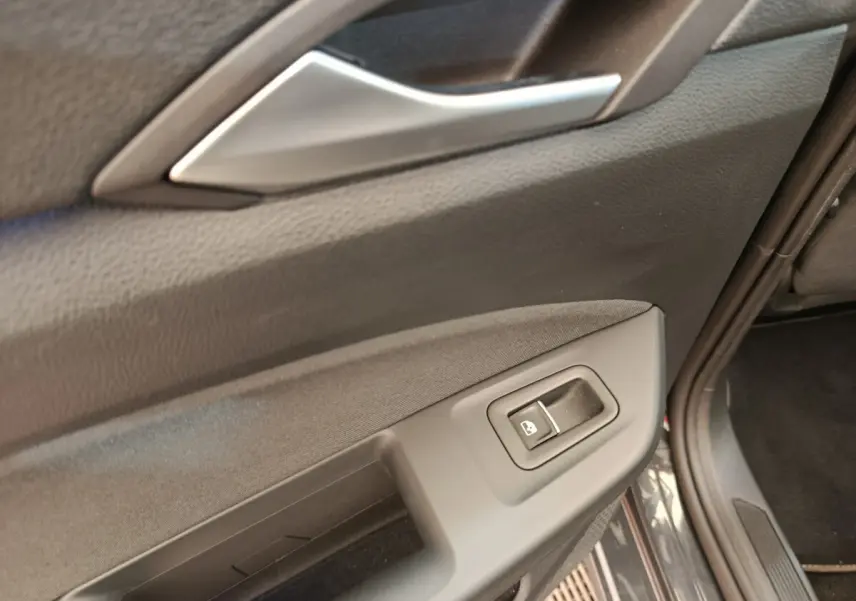 Gros plan sur la commande de lève-vitre côté conducteur de la porte intérieure d'une Volkswagen Golf gris foncé.