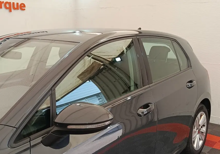Vue latérale côté gauche d'une Volkswagen Golf gris foncé avec rétroviseur et poignées de porte visibles dans un showroom.