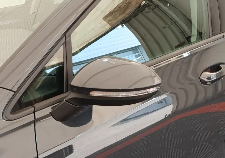 Gros plan sur le rétroviseur côté conducteur d’une Volkswagen Golf gris foncé reflétant l’environnement autour.