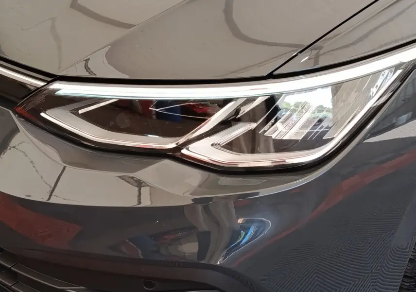 Gros plan sur le phare avant droit d'une Volkswagen Golf gris foncé, mettant en valeur ses feux LED modernes.