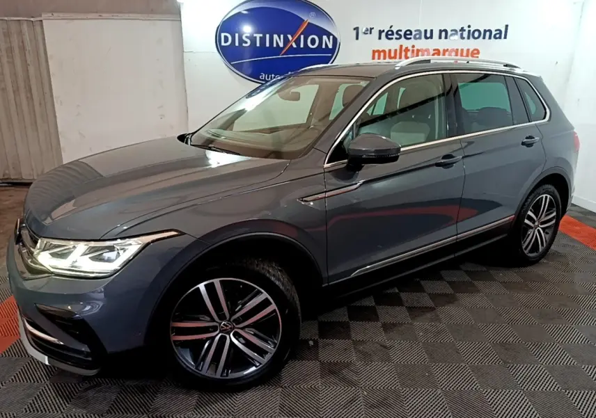 Volkswagen Tiguan gris clair vu en 3/4 avant droit, avec phares LED allumés et jantes alliage distinctives.