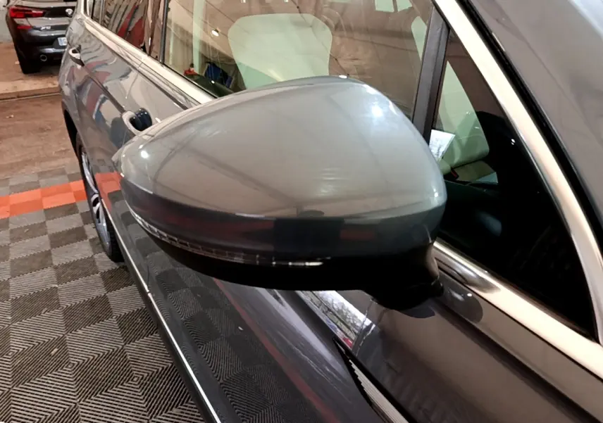 Gros plan sur le rétroviseur côté gauche gris clair du Volkswagen Tiguan 2022 dans un garage intérieur.