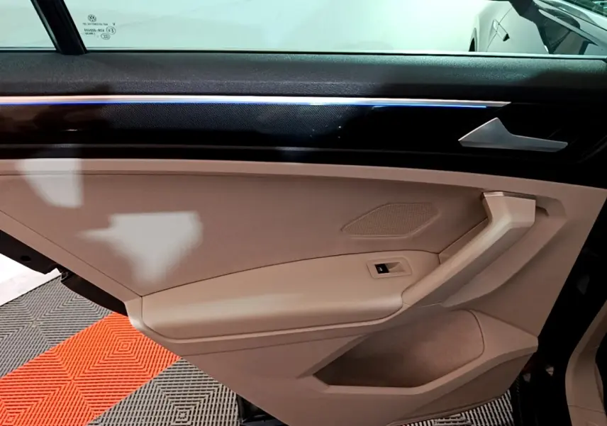 Vue intérieure du panneau de porte côté gauche beige du Volkswagen Tiguan 2022 avec éclairage d'ambiance bleu fin.