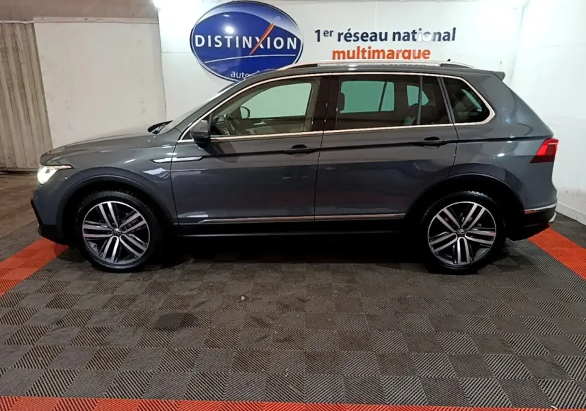 Vue latérale droite d'un Volkswagen Tiguan gris clair 2022 dans un showroom avec jantes alliage et feux allumés.