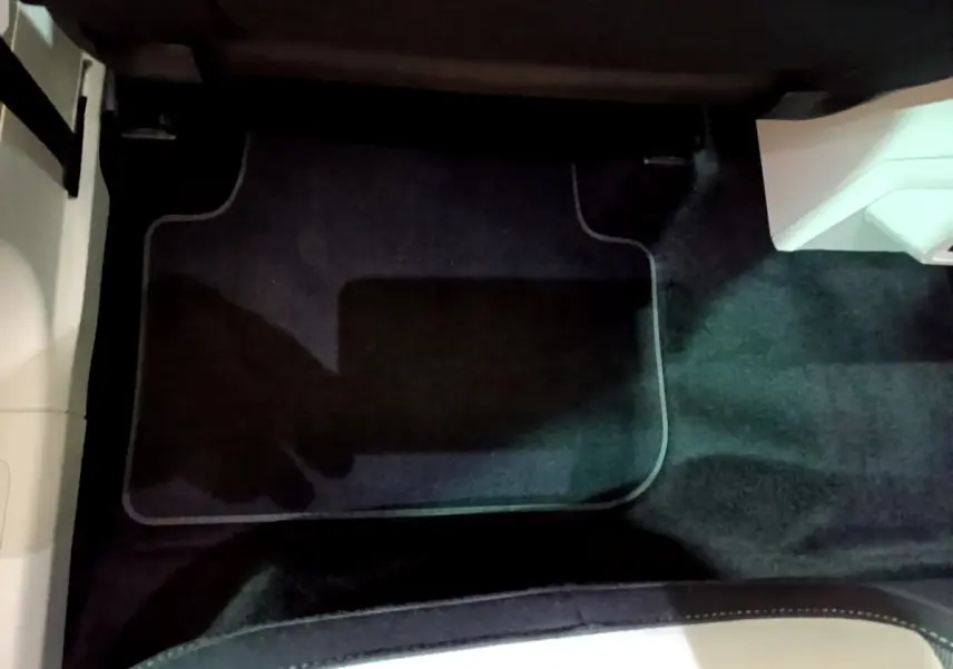 Vue du sol côté passager avant du Volkswagen Tiguan gris clair, avec tapis de sol noir et partie de la console visible.