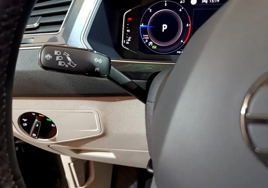 Détail intérieur du volant et levier de clignotant du Volkswagen Tiguan gris clair, avec tableau de bord numérique visible.