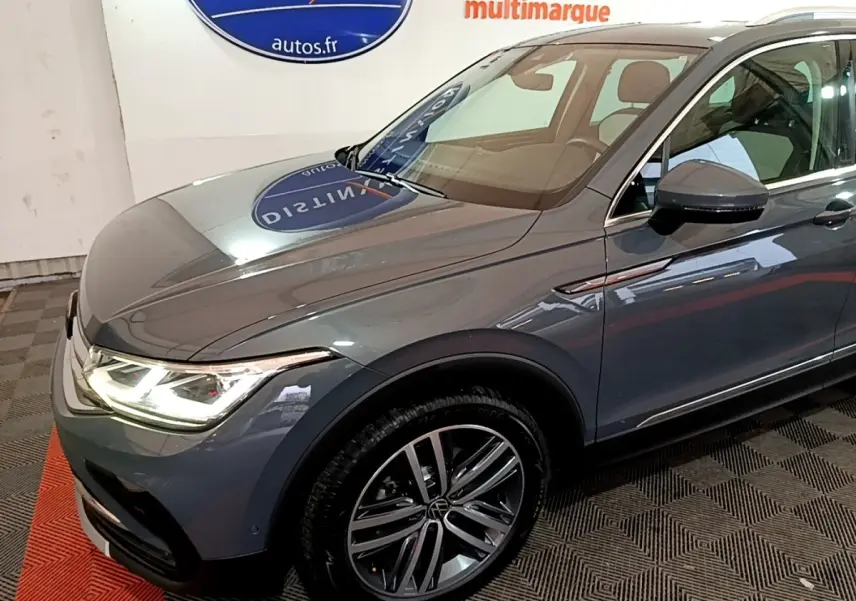 Vue 3/4 avant droit d'un Volkswagen Tiguan gris clair avec phares LED allumés et jantes alliage distinctives.