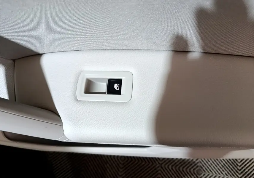 Gros plan sur le bouton de commande de vitre électrique sur la porte intérieure beige d'un Volkswagen Tiguan gris clair.