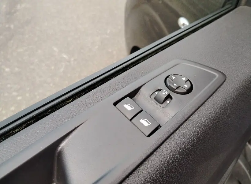 Gros plan sur les commandes de lève-vitres et rétroviseurs sur la porte côté conducteur d'un Citroën Jumpy gris titane.