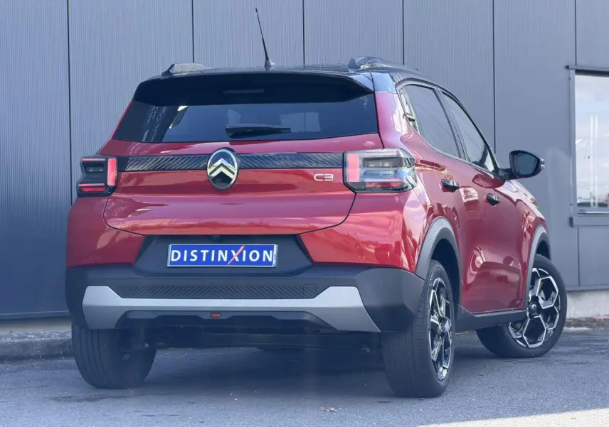 Vue 3/4 arrière droite d'une Citroën C3 2025 Rouge Elixir avec toit noir et jantes alliage distinctives.