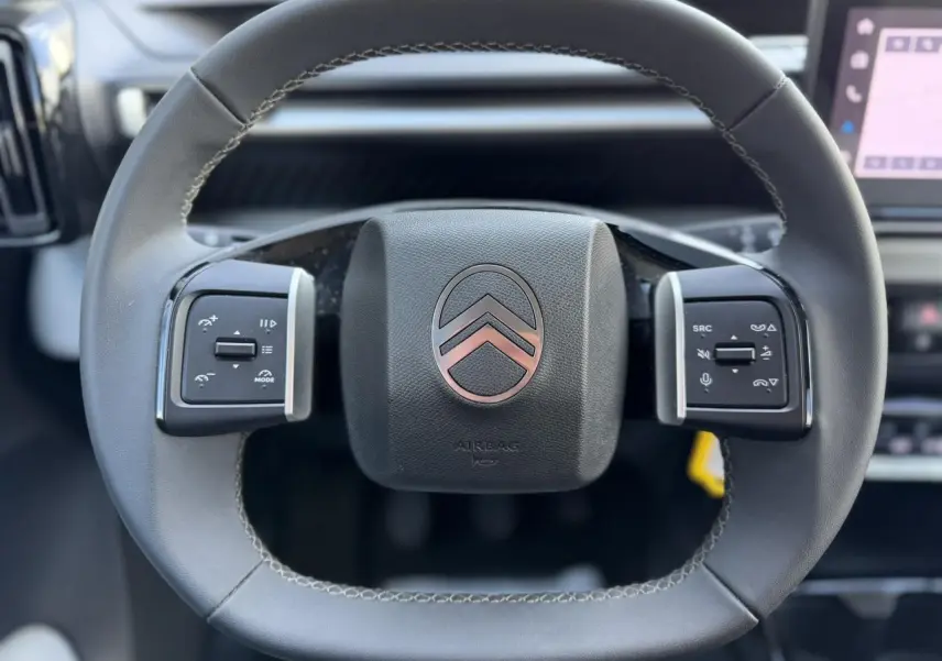 Gros plan sur le volant noir de la Citroën C3 Turbo 100 Max avec commandes intégrées et logo chromé central.