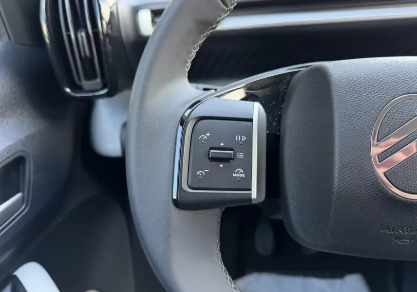 Gros plan sur la commande de régulateur de vitesse à gauche du volant noir du Citroën C3 Turbo 100 Max.