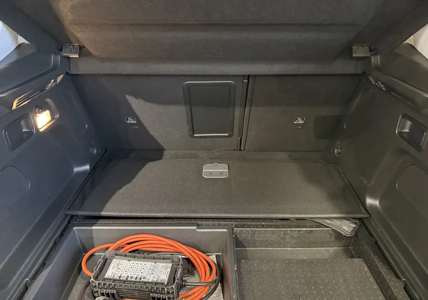 Coffre ouvert d’un Opel Grandland X blanc 2021, montrant le compartiment de rangement avec câble de recharge hybride.