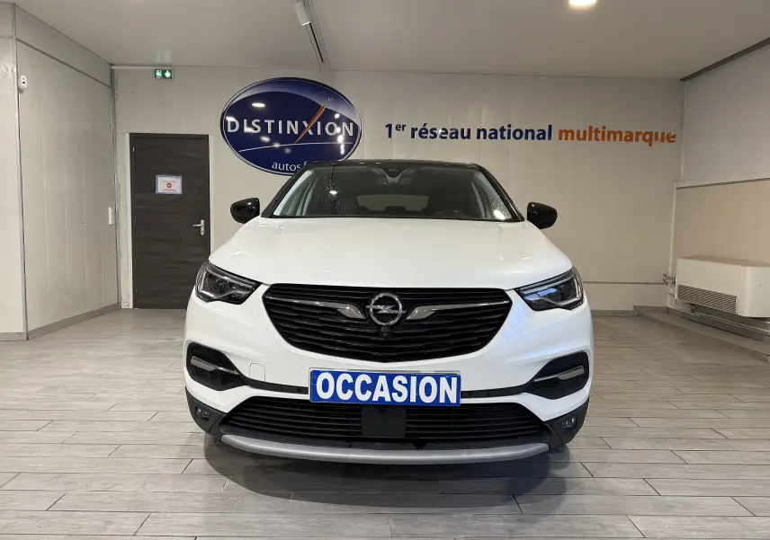 Vue frontale d'un Opel Grandland X blanc hybride rechargeable, avec calandre noire et plaque "OCCASION" en intérieur showroom.