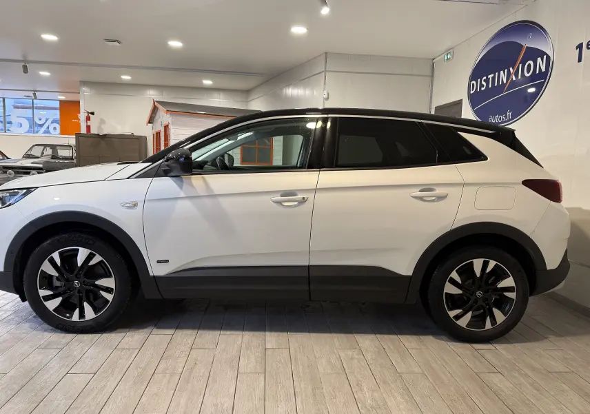 Vue de profil côté gauche d'un Opel Grandland X blanc hybride rechargeable avec toit noir et jantes bicolores en concession.