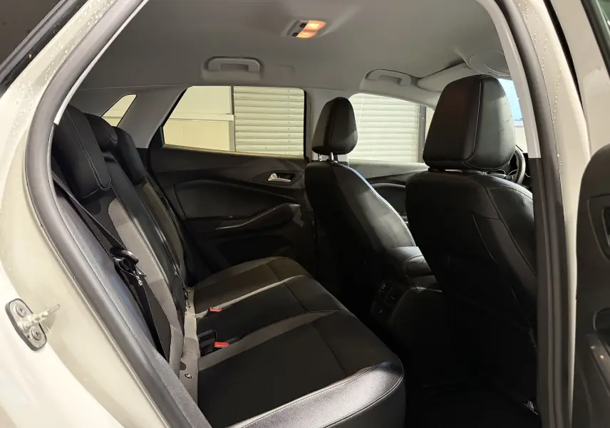Vue intérieure arrière gauche de l’Opel Grandland X blanc, montrant les sièges noirs en cuir et tissu, avec éclairage plafond allumé.