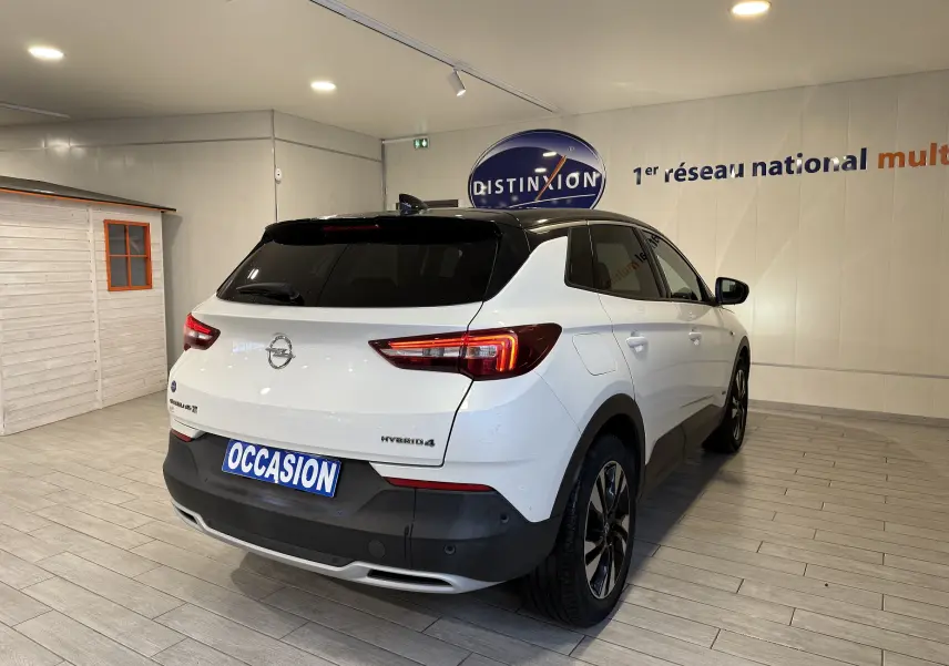 Vue 3/4 arrière droite d’un Opel Grandland X blanc hybride rechargeable avec toit noir et jantes alliage en intérieur showroom.