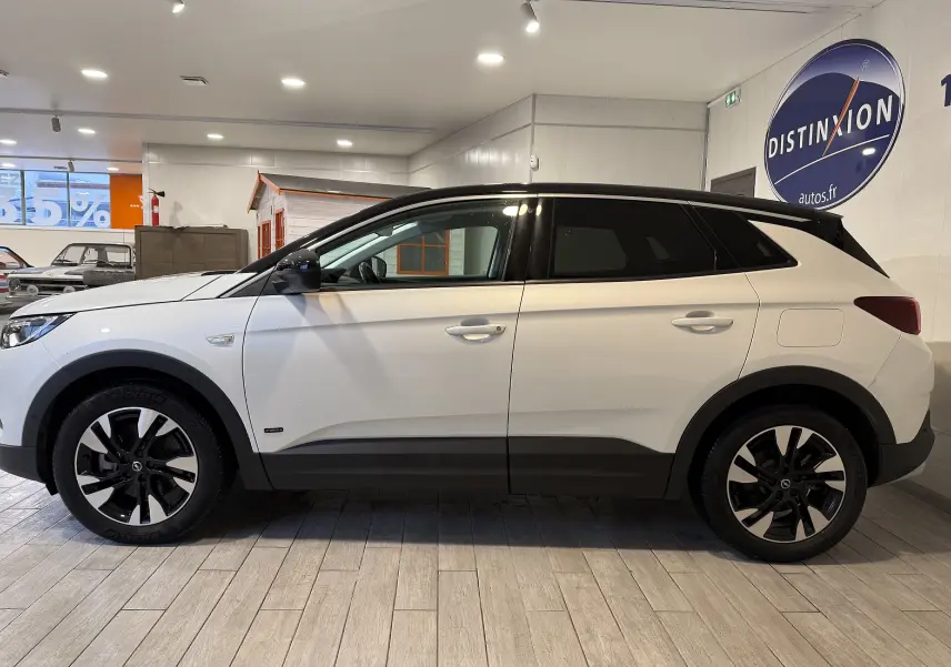 Vue de profil droit d'un Opel Grandland X blanc avec jantes noires et toit noir en intérieur showroom.