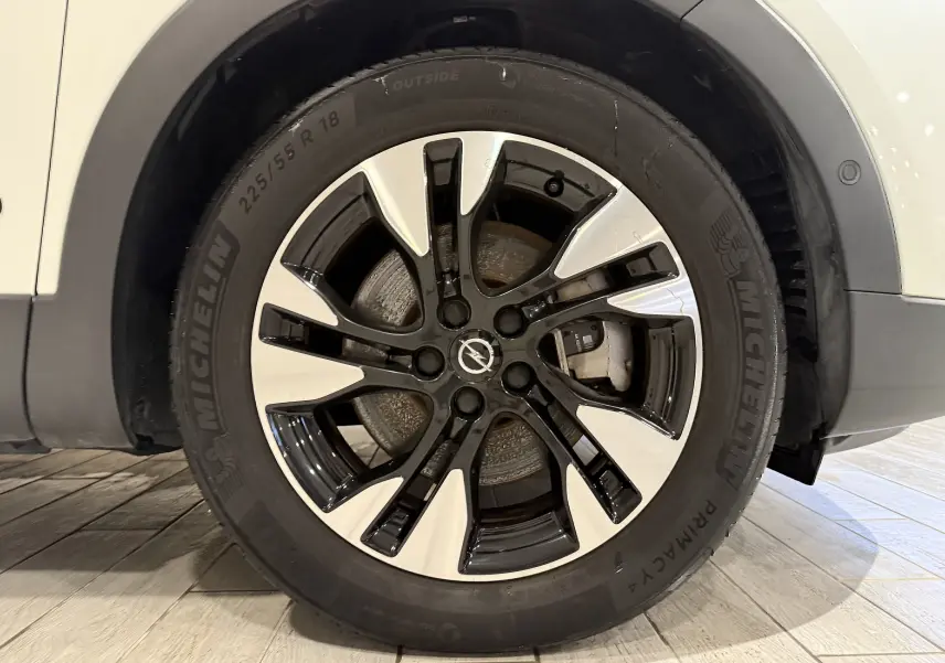 Gros plan sur la roue avant droite d’un Opel Grandland X blanc avec jante alliage bicolore noire et argent.