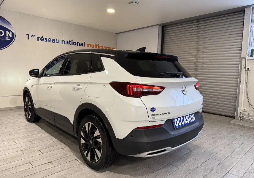 Vue 3/4 arrière droite d'un Opel Grandland X blanc avec toit noir, feux LED et jantes alliage noires.