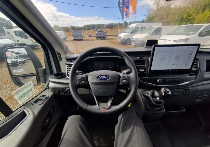 Vue intérieure du poste de conduite du Ford Transit Chassis Cabine blanc 2026, avec volant multifonction et écran tactile central.