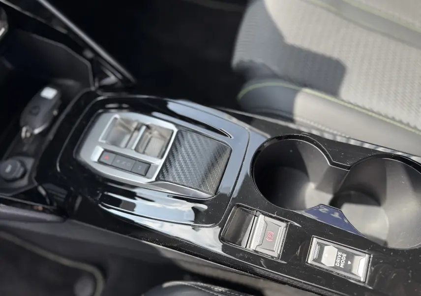 Vue rapprochée de la console centrale noire brillante de la Peugeot 208 Hybrid 145 GT avec commandes électroniques et porte-gobelets.