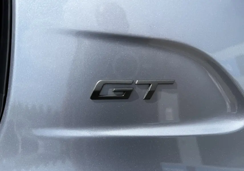 Gros plan sur l’inscription GT noire sur la carrosserie gris Artense d’une Peugeot 208 Hybrid 145 GT.