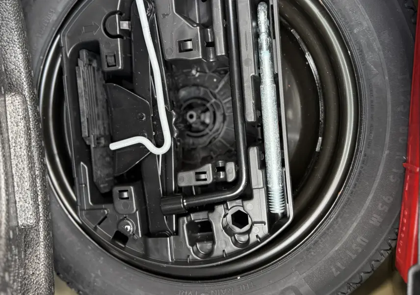 Gros plan sur la roue de secours et les outils de bord du coffre d'une Peugeot 208 Hybrid 145 GT Gris Artense 2024.