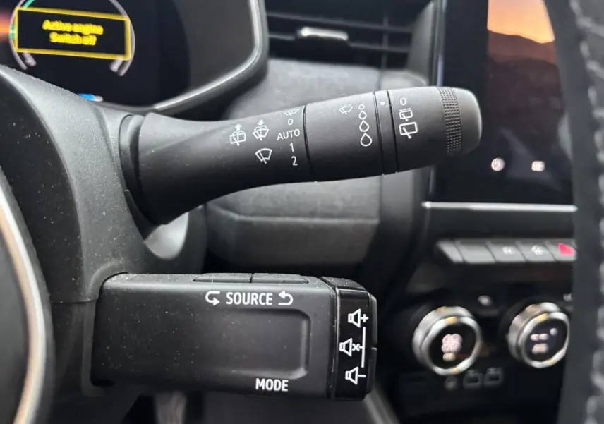 Gros plan sur les commandes au volant de la Renault Clio V hybride, avec affichage numérique partiel en arrière-plan.