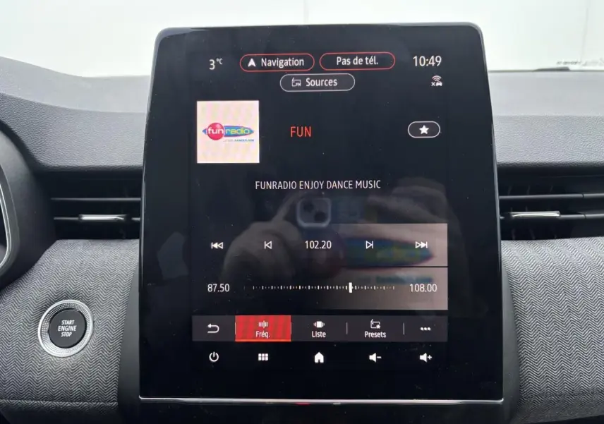 Vue rapprochée de la console centrale de la Renault Clio V rouge flamme, avec écran tactile multimédia allumé affichant la radio.