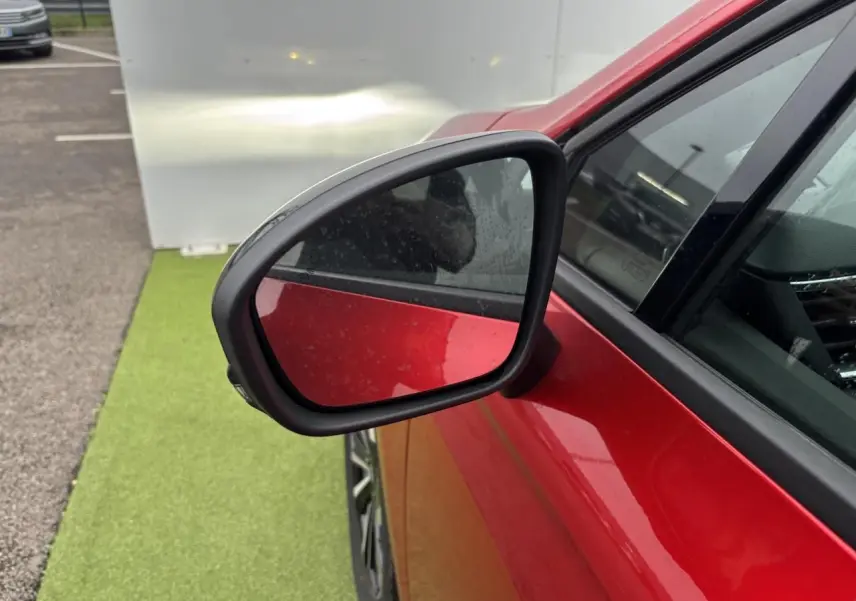 Rétroviseur côté gauche d’une Renault Clio rouge flamme métal, vue rapprochée sur la portière avant.