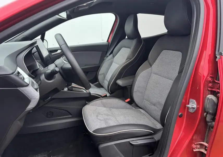 Vue intérieure côté conducteur de la Renault Clio rouge flamme, sièges tissu gris et noir avec surpiqûres claires.