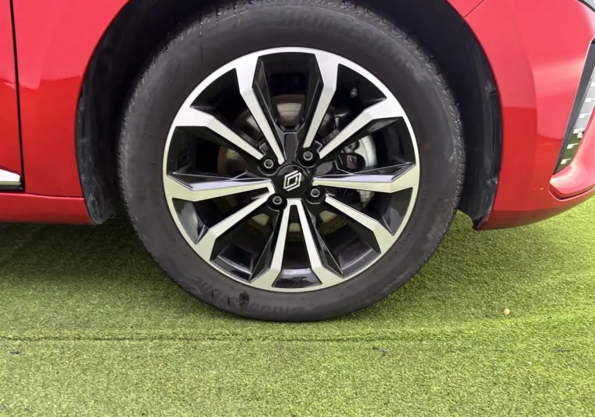 Gros plan sur la roue avant gauche avec jante alliage noire et argentée de la Renault Clio rouge flamme.