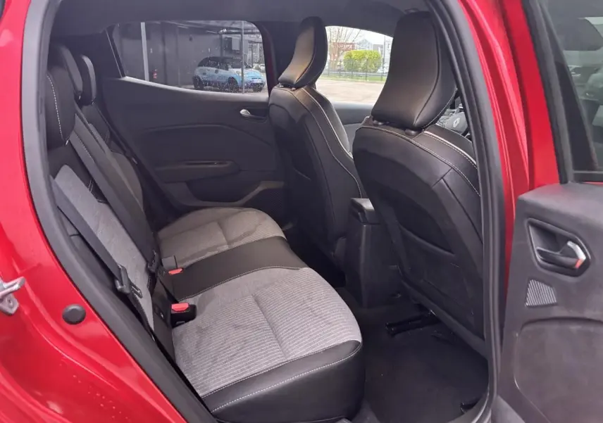 Vue intérieure arrière côté gauche de la Renault Clio V rouge flamme, montrant les sièges tissu et cuir bicolores.