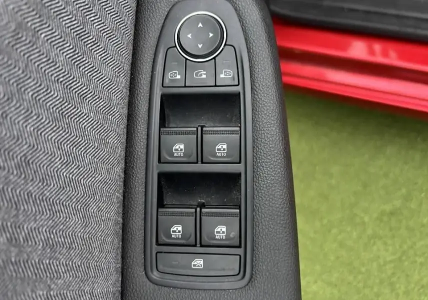 Gros plan sur les commandes des vitres électriques côté gauche avec partie de la porte rouge flamme visible en arrière-plan.