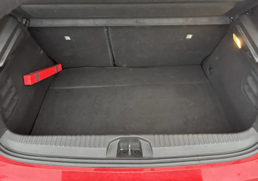 Coffre ouvert de la Renault Clio V rouge flamme, montrant un espace de rangement noir avec un triangle de signalisation.