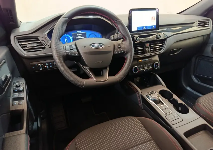 Vue intérieure avant du Ford Kuga 2024 St Line, tableau de bord noir avec écran tactile et volant cuir à surpiqûres rouges