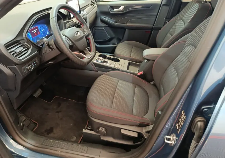 Vue intérieure côté conducteur du Ford Kuga bleu 2024, sièges tissu avec surpiqûres rouges et tableau de bord digital.
