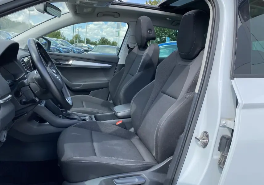 Intérieur côté conducteur d'un Skoda Karoq blanc avec sièges noirs et toit ouvrant panoramique en verre.